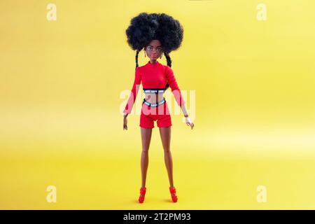 9 octobre 2023. Barnaul, Russie : poupée Barbie afro-américaine avec les cheveux noirs dans un costume rouge debout sur un fond jaune. Banque D'Images