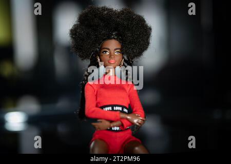 9 octobre 2023. Barnaul, Russie : poupée Barbie afro-américaine avec les cheveux noirs dans un costume rouge debout sur un fond sombre. Banque D'Images