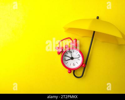 Un réveil rouge avec parapluie jaune sur fond jaune avec espace de copie. Banque D'Images