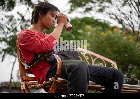 Homme javanais en chemise rouge, assis sur un banc, fond végétal avec une vue à faible angle face au ciel. Banque D'Images