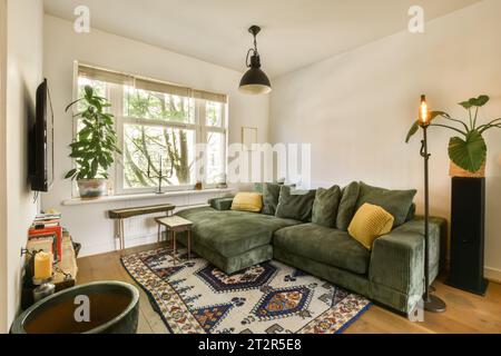 un salon avec un canapé vert et quelques plantes sur le mur derrière elle devant une grande fenêtre Banque D'Images