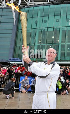 Photo de dossier datée du 24-06-2012 de Torchbearer 005 Sir Bobby Charlton tient la flamme olympique devant le stade de football Old Trafford sur le relais de la flamme entre Salford et Moss Side. Sir Bobby Charlton est mort à l'âge de 86 ans, ont annoncé sa famille. Date d'émission : samedi 21 octobre 2023. Banque D'Images