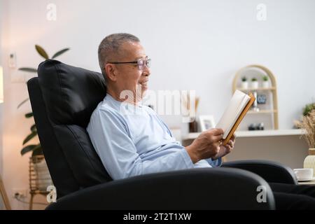 Heureux homme asiatique senior lisant le livre sur la chaise dans le salon à la maison. Banque D'Images