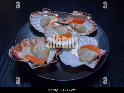 coquilles saint-jacques crues prêtes à cuire sur plaque noire et fond sombre Banque D'Images