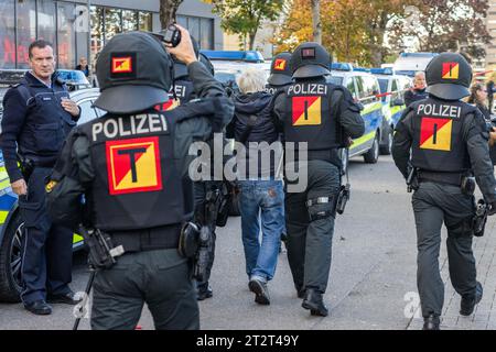 Weil am Rhein, Allemagne. 21 octobre 2023. Des policiers passent devant une rangée de véhicules de police en marge d'une manifestation intitulée «Demo pour la paix, la liberté et la souveraineté» avec un homme arrêté. Selon la police, il était difficile d'assigner les participants au rassemblement à un spectre spécifique. Entre autres, un politicien de l'AfD avait également prononcé un discours. Selon la police, les participants à la contre-manifestation viendraient du spectre de gauche. Crédit : Philipp von Ditfurth/dpa/Alamy Live News Banque D'Images