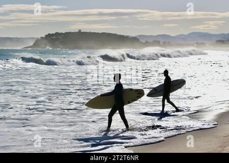 Paysage d'automne avec deux surfeurs marchant dans le surf portant des planches de surf rétro-éclairées avec la Magdalena Peninsular Sardinero Santander Cantabria Espagne Banque D'Images