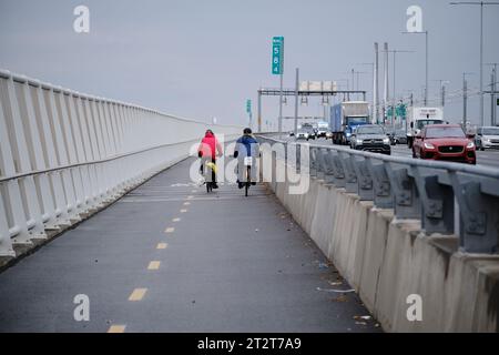 Deux cyclistes vus de derrière utilisant la piste cyclable réservée sur le pont Champlain à Montréal, tandis que la voiture passe Banque D'Images