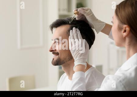 Docteur appliquant le sérum sur les cheveux du jeune homme en clinique, gros plan Banque D'Images