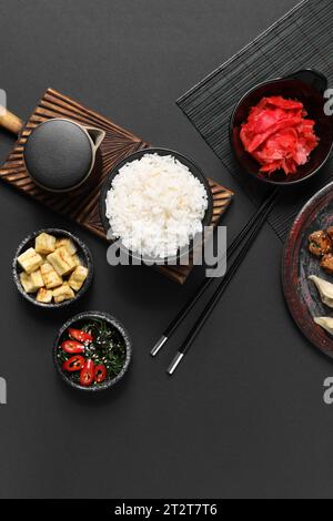 Composition avec des plats chinois savoureux et des baguettes sur fond sombre Banque D'Images