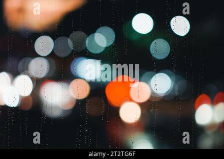 Effet bokeh des lumières de voiture avec gouttes de pluie sur le verre de fenêtre. Feux de voiture brouillés sur vitre mouillée Banque D'Images