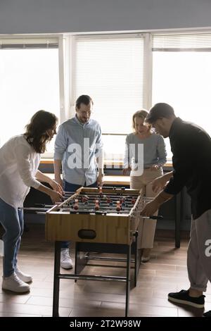 Quatre employés de bureau, amis, collègues engagés dans le jeu de baby-foot Banque D'Images