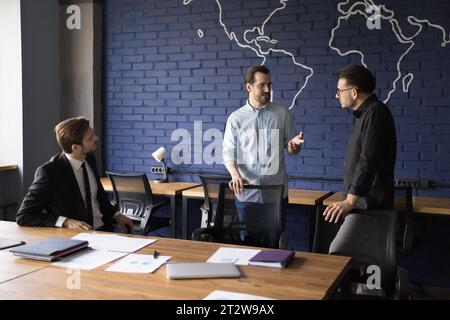 Trois hommes d'affaires millénaires négociant lors d'un briefing dans une salle de conseil moderne Banque D'Images