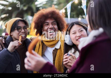 Rire des jeunes mangeant du chocolat avec des churros ensemble dans la rue dehors. Groupe multiracial. Banque D'Images