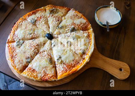 Délicieuse pizza quatro formaggi sur fond de bois avec une portion de sauce blanche sur le côté Banque D'Images