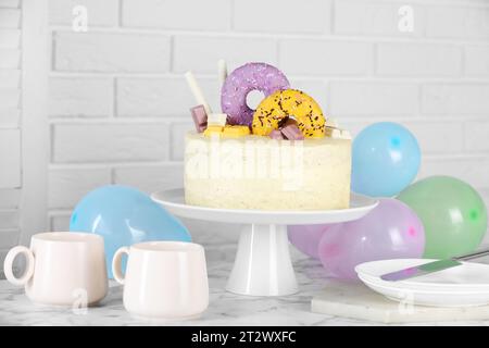 Délicieux gâteau décoré avec des bonbons, vaisselle et ballons sur la table en marbre blanc Banque D'Images