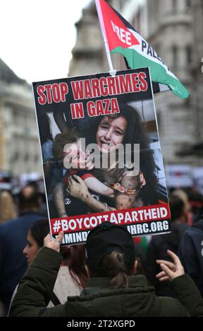 Un manifestant pro-palestinien porte une pancarte demandant "Stop aux crimes de guerre à Gaza" alors qu'ils marchent à travers Londres. Les partisans de la Palestine se réunissent pour marcher vers Downing Street après les bombardements israéliens et la menace d’une invasion terrestre de Gaza par les forces israéliennes. C'est la deuxième semaine consécutive que plus de 100 000 personnes sont descendues dans les rues de Londres pour protester. De nombreuses organisations impliquées ont lancé un appel général pour un cessez-le-feu, l'ouverture du terminal de Rafah en Égypte et l'autorisation de l'aide humanitaire dans la bande de Gaza. Banque D'Images