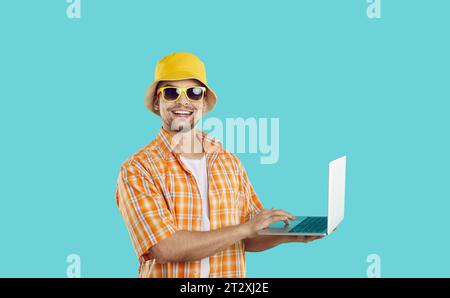 Happy man utilise un ordinateur portable pour trouver une visite d'été, réserver un hôtel ou travailler en ligne pendant les vacances. Banque D'Images