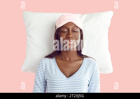 Jeune femme afro-américaine dormant paisiblement sur un oreiller blanc isolé sur un fond rose Banque D'Images