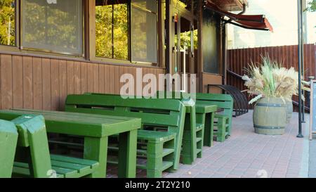 terrasse vide d'un bar ou d'un café avec des meubles en bois massif vert rugueux debout près d'un mur brun avec des fenêtres de la chambre Banque D'Images