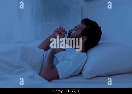 Vue latérale de l'homme indien malade toussant dans le lit dans la nuit Banque D'Images