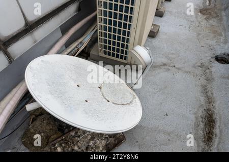 Antenne parabolique dysfonctionnelle et jetée couchée sur le sol, une métaphore visuelle de l'abandon et de la délabrement Banque D'Images
