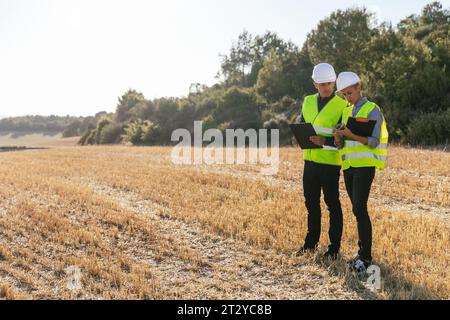 Une équipe d'ingénieurs debout sur le terrain regardant des plans sur un téléphone portable. Banque D'Images