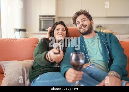 Un jeune couple profite d’un moment de connexion dans un salon. L'homme, dans un sweat à capuche sarcelle, et la femme, dans un pull vert foncé, tiennent tous les deux des lunettes de Banque D'Images