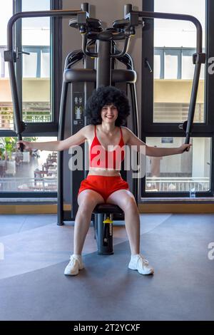 Femme avec les cheveux bouclés dans la salle de gym faisant des exercices de sports de force. Banque D'Images