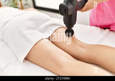 Jeune femme caucasienne couchée sur la table ayant massage des jambes à l'aide d'un pistolet à percussion au salon de beauté Banque D'Images