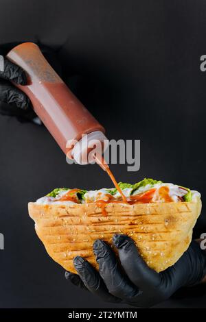 Cuisiniers à la main ajoutant de la sauce au doner kebab à travers des trous déchirés sur fond de papier noir Banque D'Images