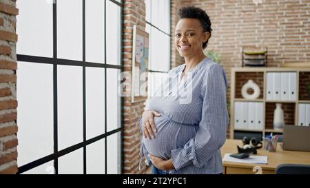 Jeune femme enceinte travailleur d'affaires souriant confiant touchant le ventre au bureau Banque D'Images
