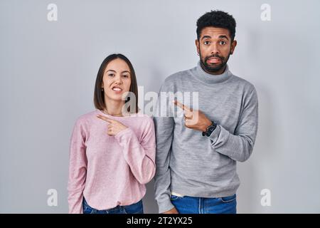 Jeune couple hispanique debout ensemble montrant de côté inquiet et nerveux avec index, expression concernée et surprise Banque D'Images