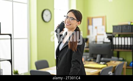 Jeune belle femme hispanique travailleur d'affaires souriant confiant tenant le café au bureau Banque D'Images