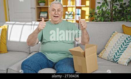 Homme d'âge moyen aux cheveux gris déballant une boîte en carton faisant un geste de pouce vers le haut à la maison Banque D'Images