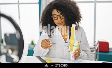 Femme afro-américaine traumatologue médecin enregistrant vidéo tutoriel du genou à la clinique Banque D'Images