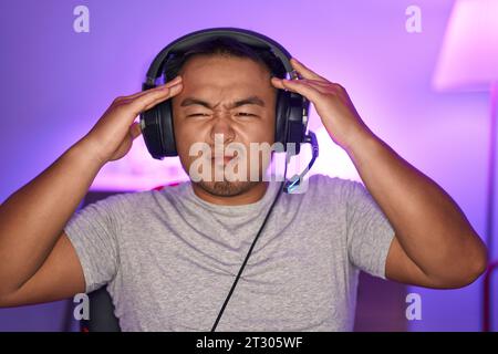 Jeune homme chinois jouant à des jeux vidéo portant un casque avec la main sur la tête, mal de tête parce que le stress. souffrir de migraine. Banque D'Images