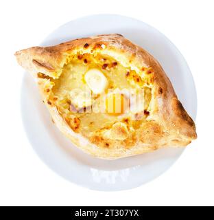 Plat géorgien traditionnel de pain fourré au fromage - khachapuri dans le style adjarien avec oeuf et beurre sur plaque blanche isolé sur fond blanc Banque D'Images