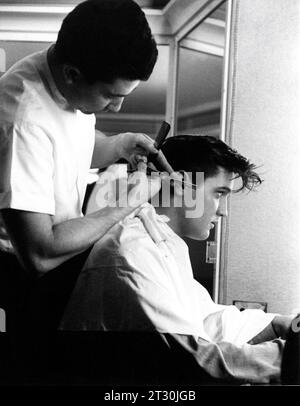 ELVIS PRESLEY se fait couper les cheveux par le coiffeur / barber RAMIRO JALOMA aux Paramount Studios à Hollywood lors du tournage de LOVING YOU 1957 réalisateur HAL KANTER Hal B. Wallis Productions / Paramount Pictures Banque D'Images