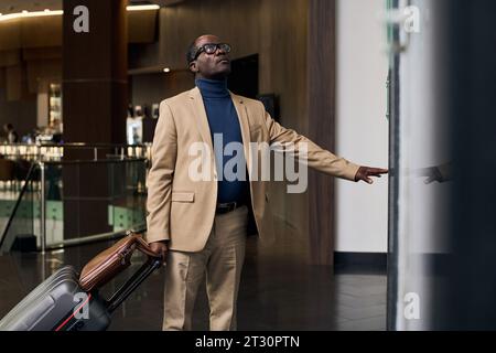 Homme afro-américain avec des bagages appuyant sur le bouton et attendant l'ascenseur Banque D'Images