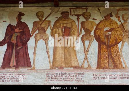 Des squelettes souriants se tiennent debout avec un prêtre (à gauche), un frère et un imperateur ou un empereur en robe dorée, chaque homme percé par la flèche de la mort. Détail de la fresque Renaissance Danza Macabra (danse de la mort), peinte en 1539 par Simone II Baschenis (c. 1495-1555) sur un mur extérieur de la Chiesa di San Vigilio à Pinzolo, Trentin-Haut-Adige, Italie. La frise a des légendes en dialectes locaux et en langue vernaculaire comprise par les gens ordinaires. Banque D'Images
