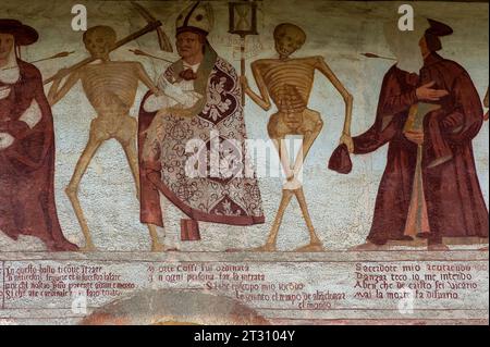 Détail de la frise de fresque Danza Macabra (danse de la mort) du XVIe siècle : des squelettes souriants se dressent avec un cardinal (partiellement visible à gauche), évêque et prêtre, chaque pasteur percé d'une flèche de mort. Peint par l'artiste italien Simone II Baschenis (v. 1495-1555) sur le mur extérieur de la Chiesa di San Vigilio à Pinzolo, Trentin-Haut-Adige, Italie. La frise a des légendes en dialectes locaux et en langue vernaculaire comprise par les gens ordinaires. Banque D'Images