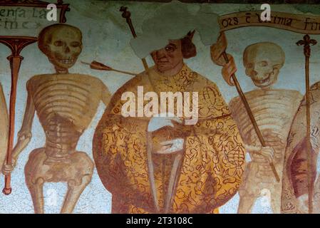 Détail de la frise de fresque Danza Macabra (danse de la mort) du XVIe siècle : deux squelettes avec des sourires dentelés flanquent un imperator ou empereur en robe dorée qui est percé par une flèche de mort. Peint par l'artiste italien Simone II Baschenis (v. 1495-1555) sur le mur extérieur de la Chiesa di San Vigilio à Pinzolo, Trentin-Haut-Adige, Italie. Banque D'Images