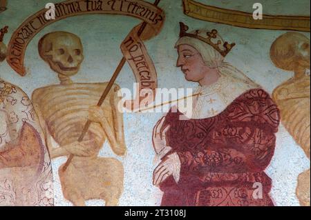 Détail de la frise de fresque Danza Macabra (danse de la mort) du 16ème siècle : squelette souriant se dresse avec la reine qui est percée par la flèche de la mort. Peint par l'artiste italien Simone II Baschenis (v. 1495-1555) sur le mur extérieur de la Chiesa di San Vigilio à Pinzolo, Trentin-Haut-Adige, Italie. Banque D'Images