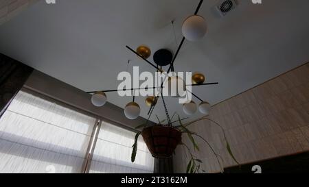 Un petit lustre moderne contre un plafond blanc et un pot de fleurs suspendu avec une plante verte. Créatif. Eléments décoratifs d'appartement. Banque D'Images