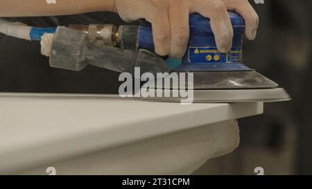 Gros plan de la planche en bois de polissage principale. Créatif. Machine de polissage dans les mains du maître de travail du bois. Homme polit la table en bois avec la machine dans Banque D'Images