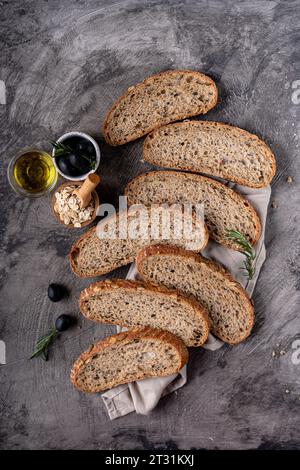 Pain au levain cuit au four à partir de farine de grains entiers et de graines de citrouille sur une grille, huile d'olive et olive noire sur une table en bois rustique. Pain artisanal. Banque D'Images