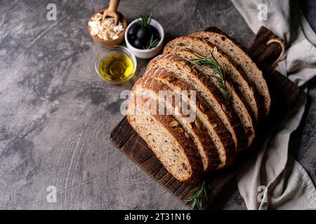 Pain au levain cuit au four à partir de farine de grains entiers et de graines de citrouille sur une grille, huile d'olive et olive noire sur une table en bois rustique. Pain artisanal. Banque D'Images