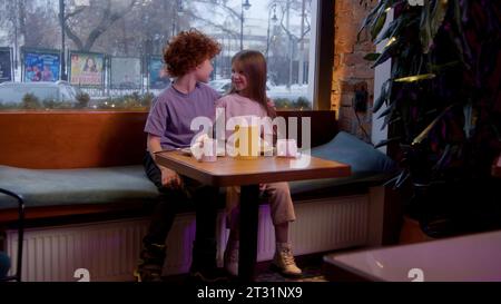 Un rendez-vous pour enfants dans un café. Film. Des vacances d'enfants où un garçon donne une peluche à une fille et ils boivent du cacao chaud. Banque D'Images