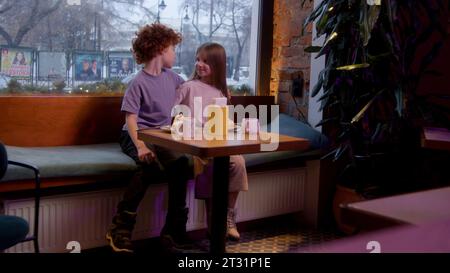 Un rendez-vous pour enfants dans un café. Film. Des vacances d'enfants où un garçon donne une peluche à une fille et ils boivent du cacao chaud. Banque D'Images