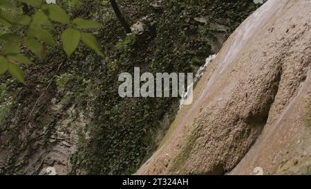 Vue de côté rapprochée de la cascade coulant sur le rocher. Créatif. Beau petit ruisseau d'eau coule en bas de falaise de pierre dans la forêt. Vue latérale de belle Banque D'Images